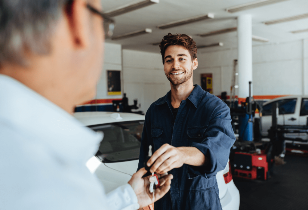 A mechanic in a garage handing over keys to a customer, having just used a car key programming tool to fix the customer's keys.